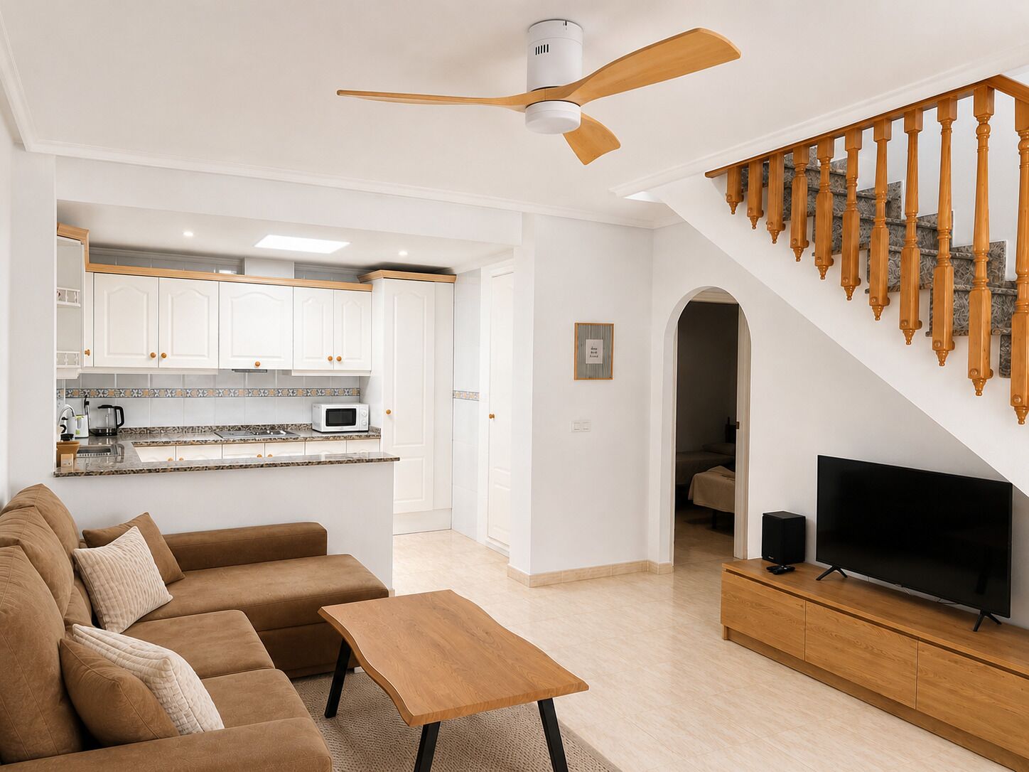 A modern living room with a sofa, a coffee table, a TV, and a staircase with wooden balusters.
