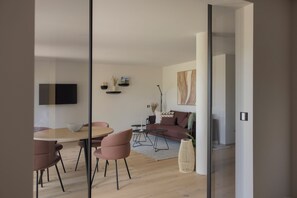 A modern living space with a dining area, a sofa, and a television mounted on the wall. - Sona Suites Allgäu: Sauna, Hot Tub, and Views of Nature (Wiggensbach)