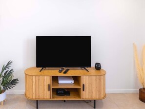 Un meuble de rangement en bois pour appareils multimédias, comprenant un téléviseur à écran plat, des télécommandes et une console de jeux.