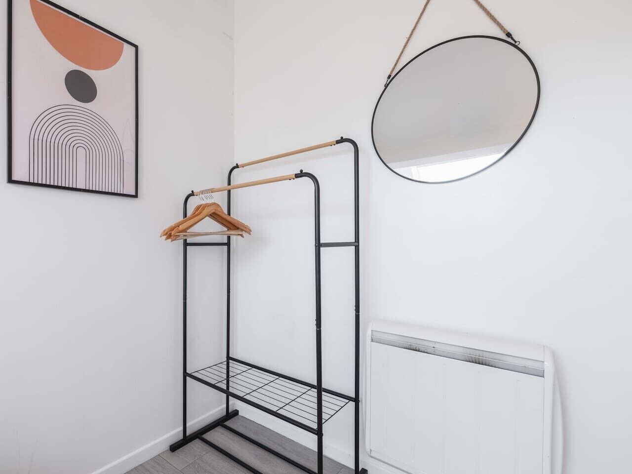 Une pièce avec un étagère en métal, un miroir rond et un radiateur.