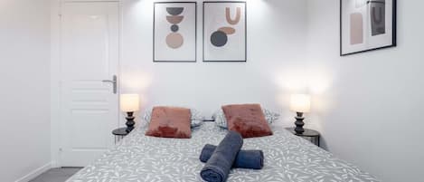 Un dormitorio con una cama, dos lámparas de noche, una puerta y dos obras de arte colgadas en la pared.