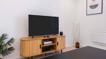 Ein modernes Wohnzimmer mit Flachbildfernseher auf einer Holzkassette, einem schwarzen Couchtisch und einer Topfpflanze.