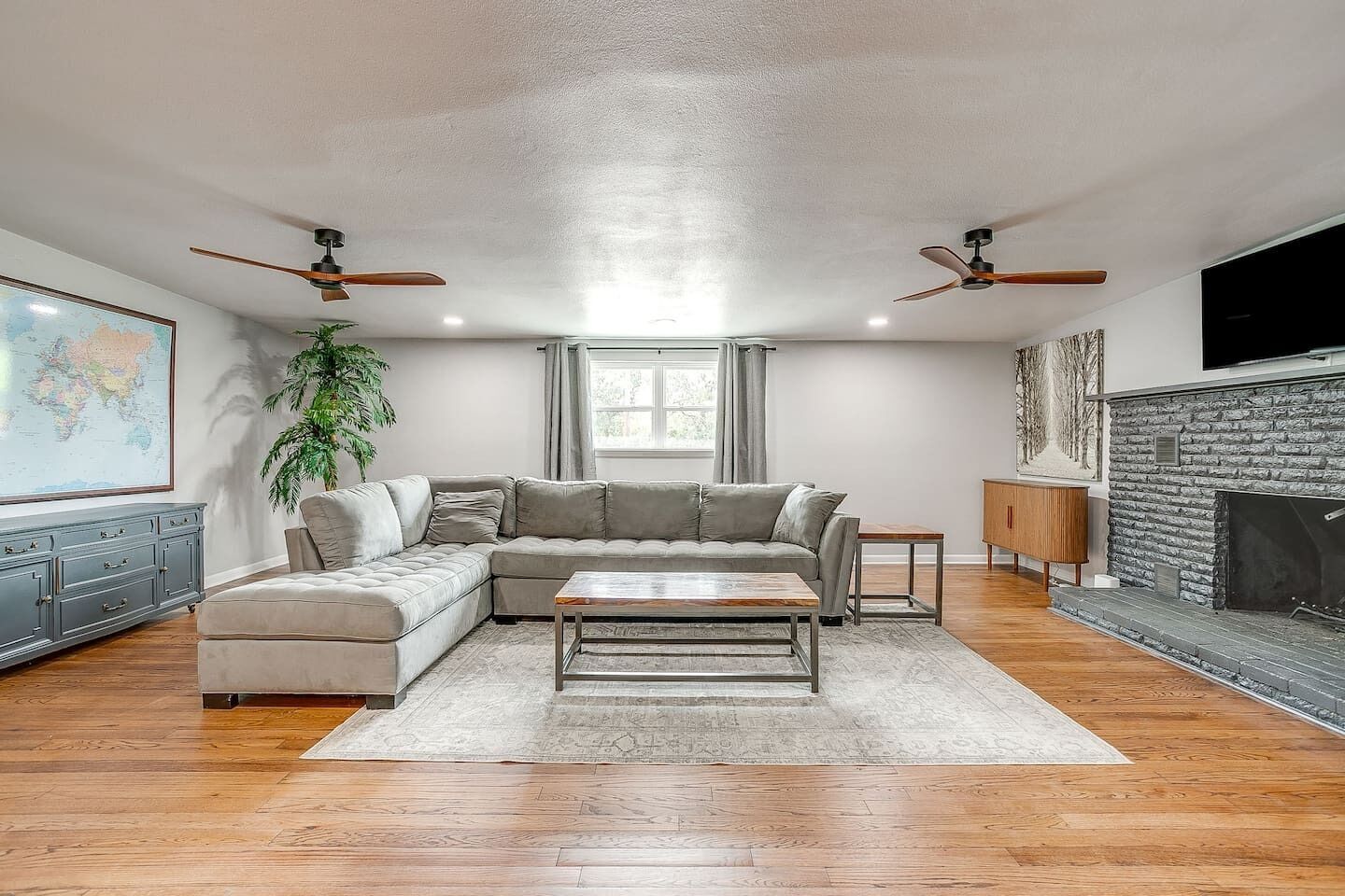 Ein Wohnzimmer mit Ecksofa, Couchtisch, Kamin, Fernseher und Deckenventilatoren.