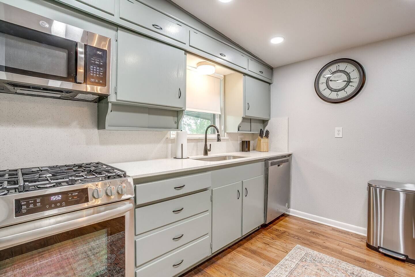 A kitchen with a stainless steel stove, a microwave, a sink, and a clock on the wall.