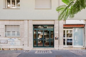 Um edifício com porta e janelas verdes, uma porta de garagem visível e uma árvore em primeiro plano.