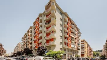 Un edificio residencial de varios pisos con balcones, un estacionamiento al frente y un cielo despejado.
