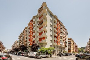 Un edificio residencial de varios pisos con balcones, un estacionamiento al frente y un cielo despejado.