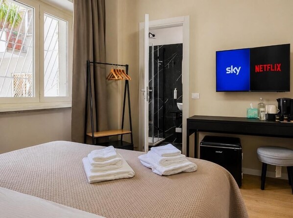 Habitación de hotel con cama, escritorio, televisor que muestra Sky y Netflix, y zona de ducha.