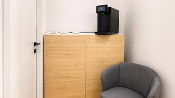 Una habitación con un armario de madera, una silla gris y una cafetera negra.