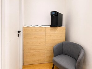 Una habitación con un armario de madera, una silla gris y una cafetera negra.