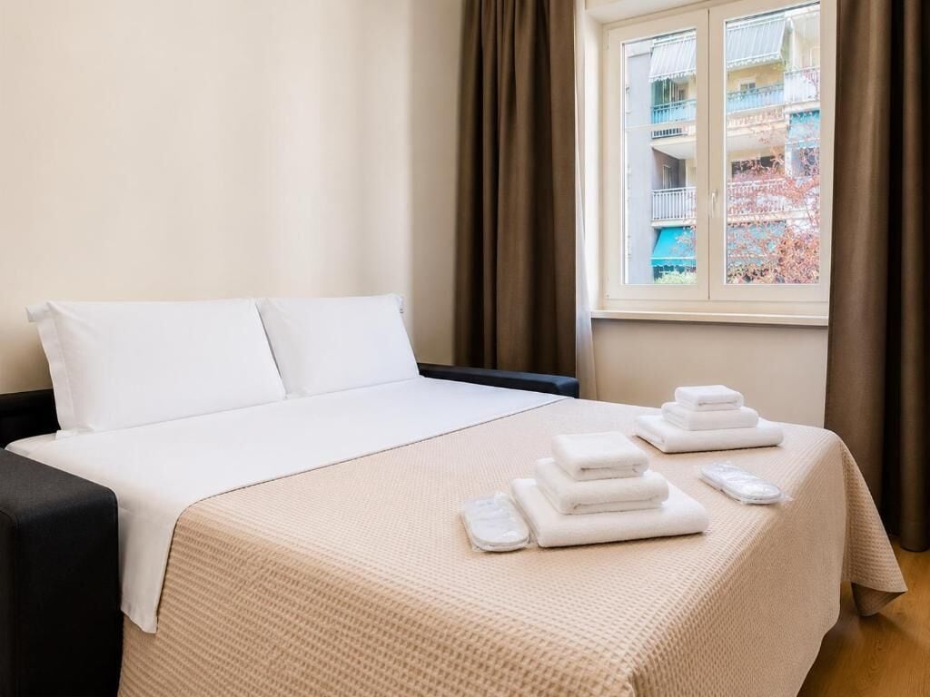 A hotel room with a bed, a window with curtains, and a view of a building outside.