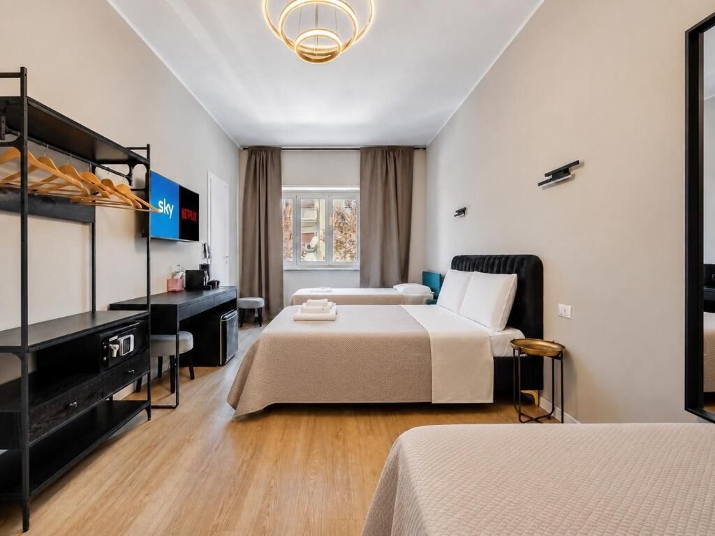 A hotel room with two beds, a desk, a TV, and a window with curtains.