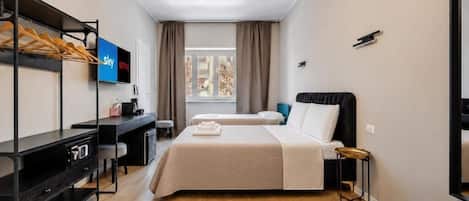 A hotel room with two beds, a desk, a TV, and a window with curtains.
