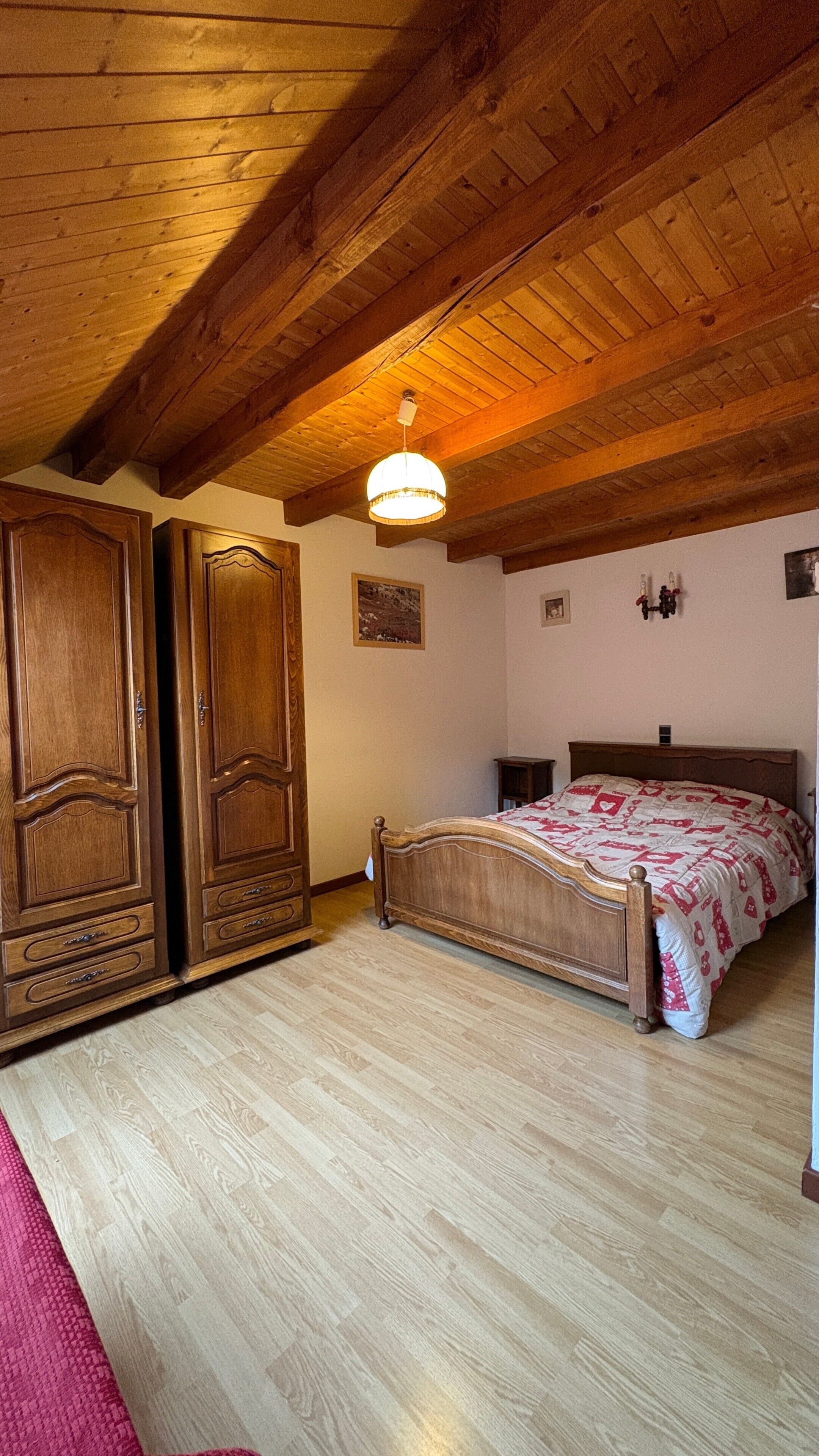 Une chambre avec un plafond en bois, un lit recouvert d’une couvre-lit à motifs et une armoire.