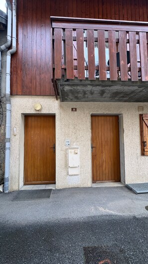 Un bâtiment doté de deux portes en bois, d’un petit coffret de raccordement électrique et d’un balcon avec des balustrades en bois.