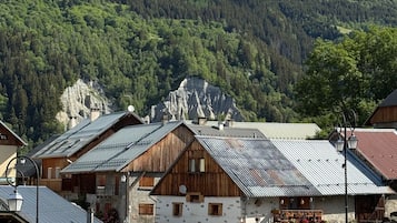 Een bergdorpslandschap met traditionele houten gebouwen, een verharde weg en een achtergrond van ruige bergen.