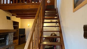 A wooden staircase leading to a loft area with a fireplace, a television, and a framed picture on the wall.