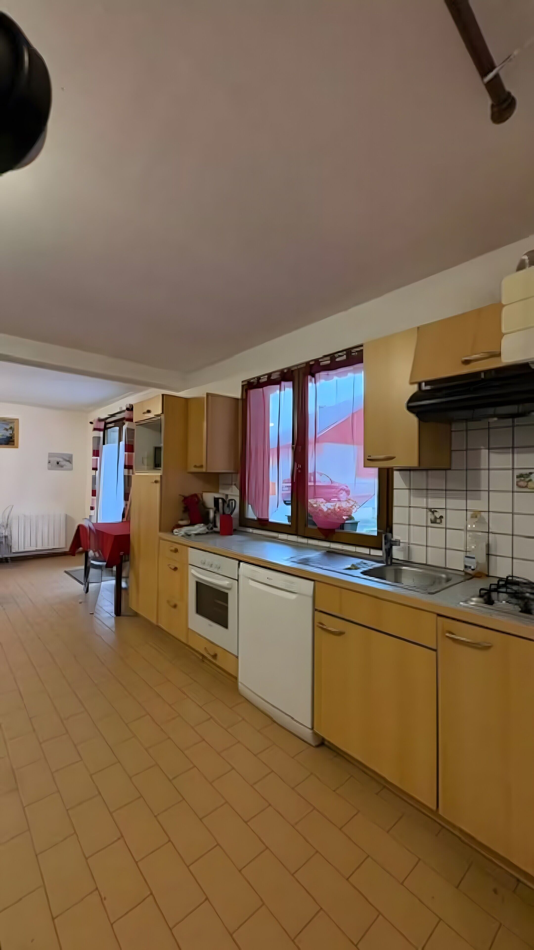 Une cuisine avec des meubles en bois, un lave-vaisselle, une cuisinière et une fenêtre avec des rideaux.