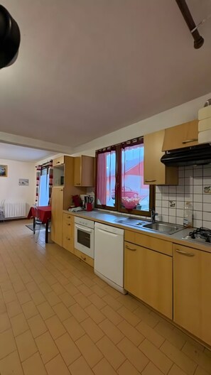 A kitchen with wooden cabinets, a dishwasher, a stove, and a window with curtains. - Apartment 'Logement Entier 6 Couchages Wifi' with Wi-Fi (Saint François Longchamp)