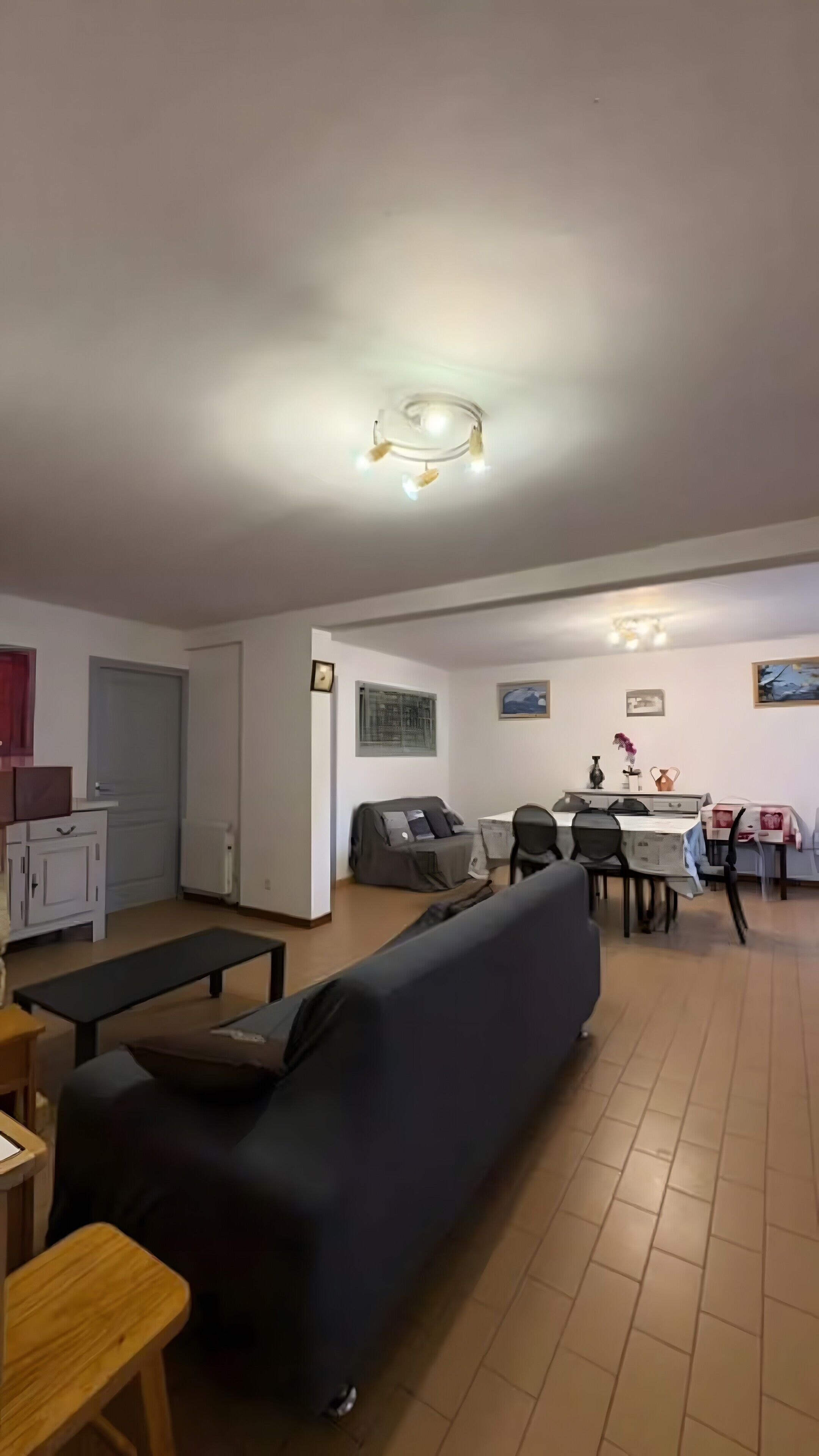Un salon comprenant un canapé, une table à manger avec des chaises, un banc et un luminaire suspendu au plafond.