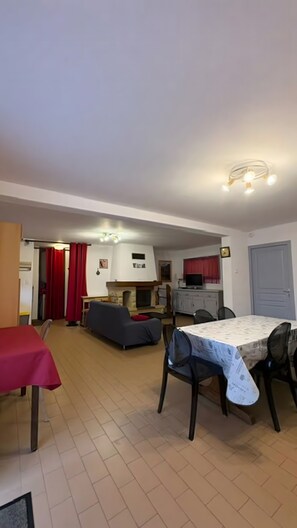 A living room with a fireplace, a dining area with a table and chairs, and a kitchen area with a TV and cabinets.