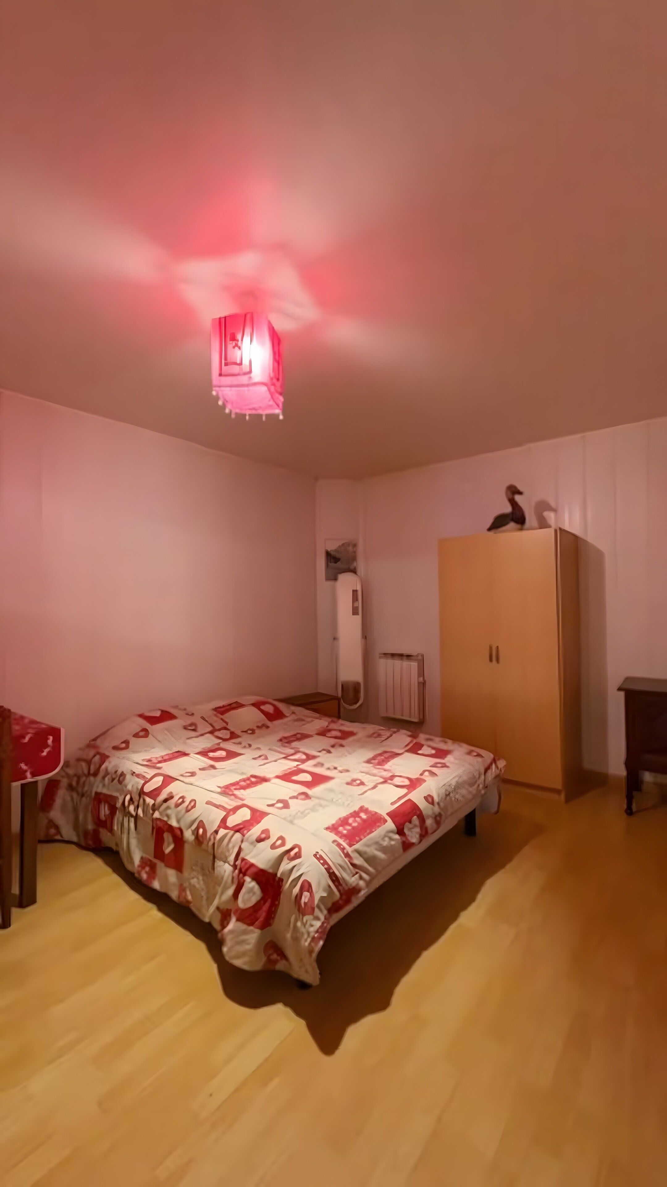 A bedroom with a bed, a wardrobe, a radiator, and a hanging light fixture.