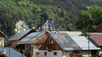 Un pueblo de montaña con casas de madera tradicionales, una carretera pavimentada y montañas escarpadas al fondo.