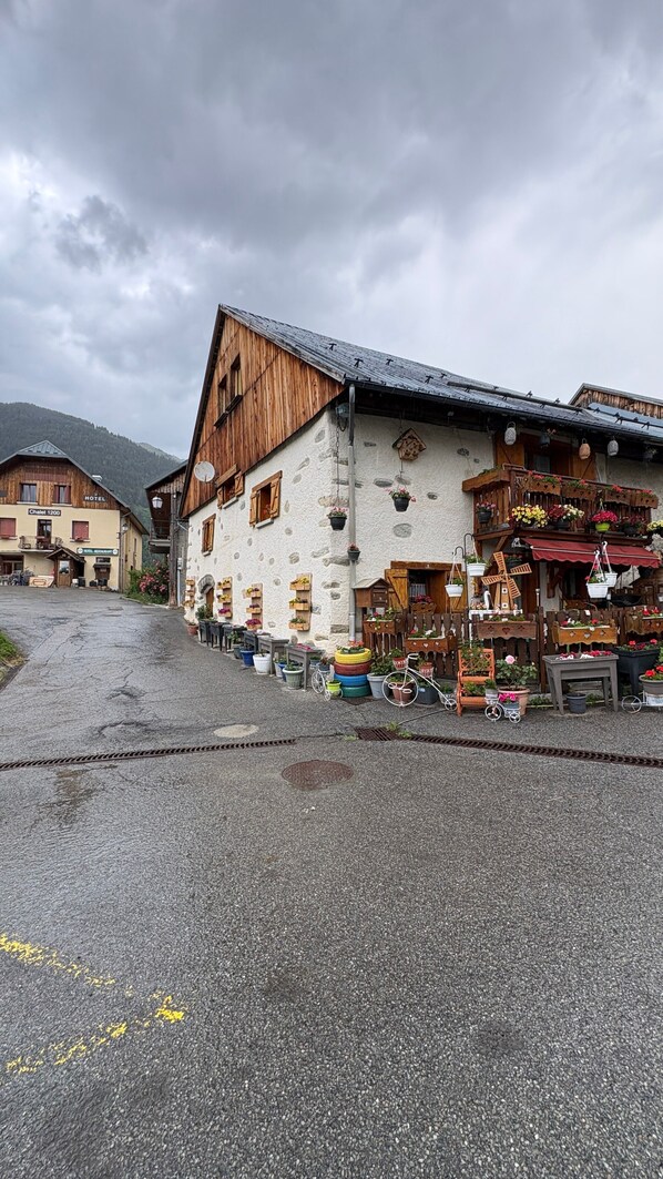 A traditional wooden building with a sloped roof, a stone facade, and a ground floor with a variety of potted plants and outdoor seating.