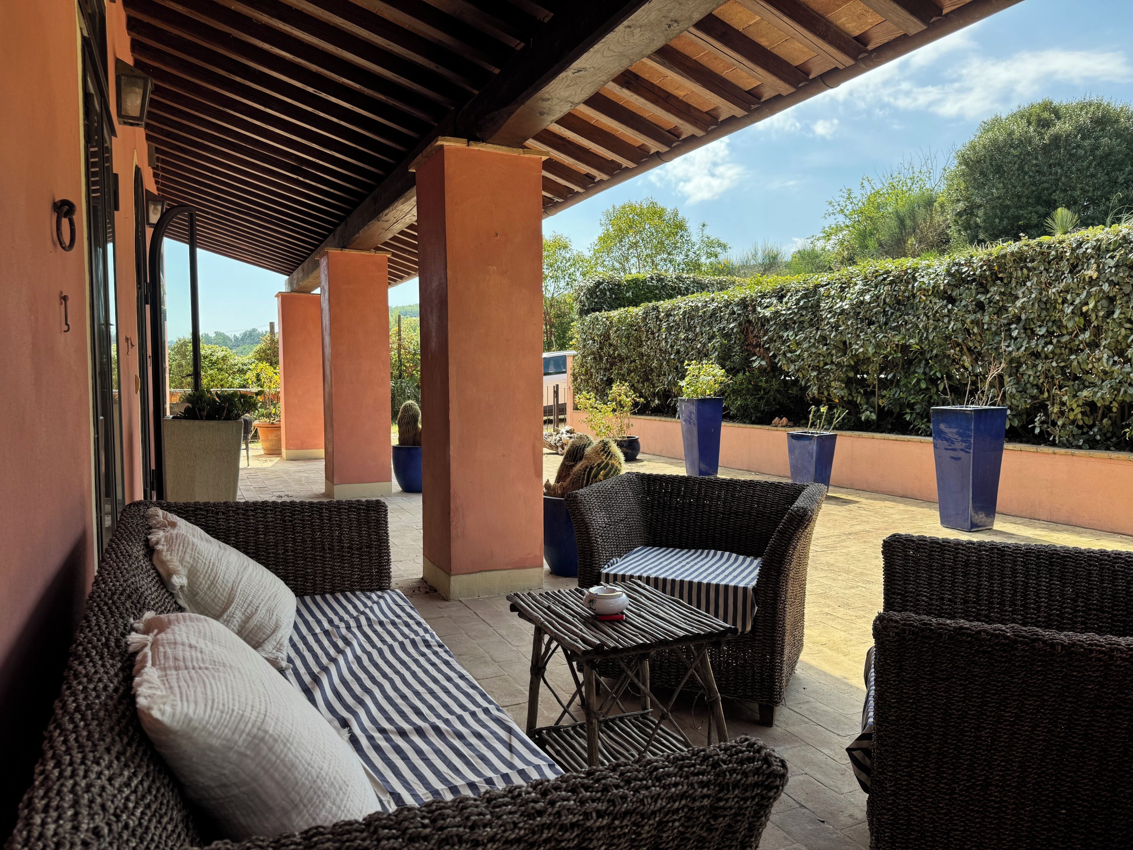 An outdoor patio with wicker furniture, potted plants, and a view of the surrounding greenery.
