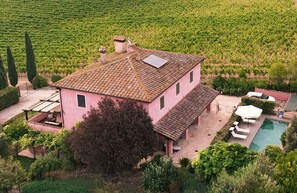 A two-story house with a tiled roof, a swimming pool, and a vineyard in the background. - Podere Gora (Toscana)