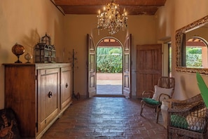 A hallway with a chandelier, wooden cabinets, and a wicker chair. - Podere Gora (Toscana)