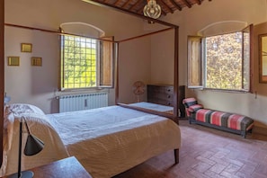 A room with a four-poster bed, a bench, a radiator, and a window with a view of trees. - Podere Gora (Toscana)