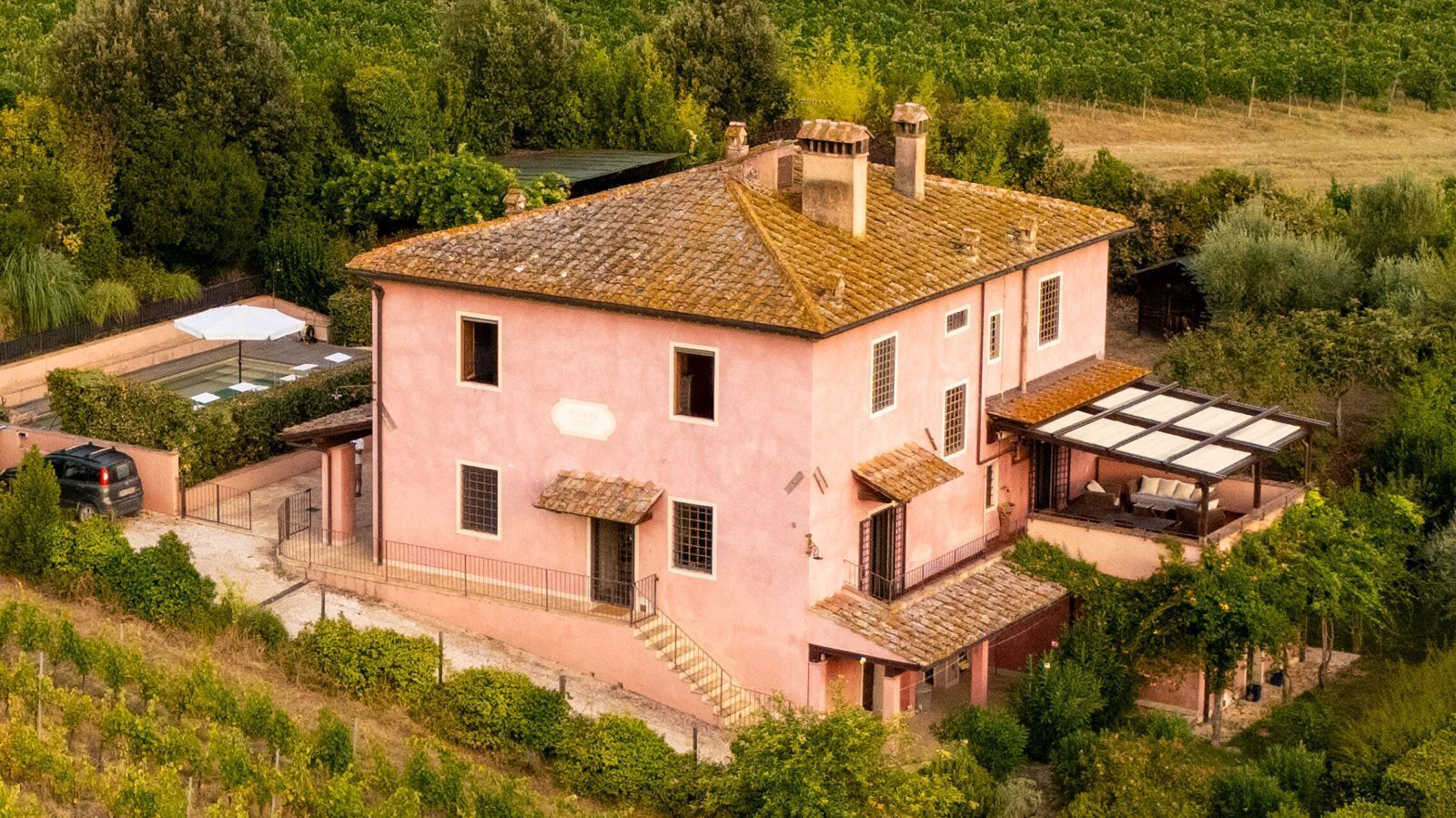 Una villa rosa con techo de tejas, un porche cubierto y un jardín.
