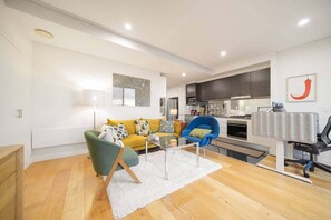 Ein stilvoller Wohnraum mit Sofa, Sessel, Couchtisch und Küchenzeile inklusive Schränken und Geräten.