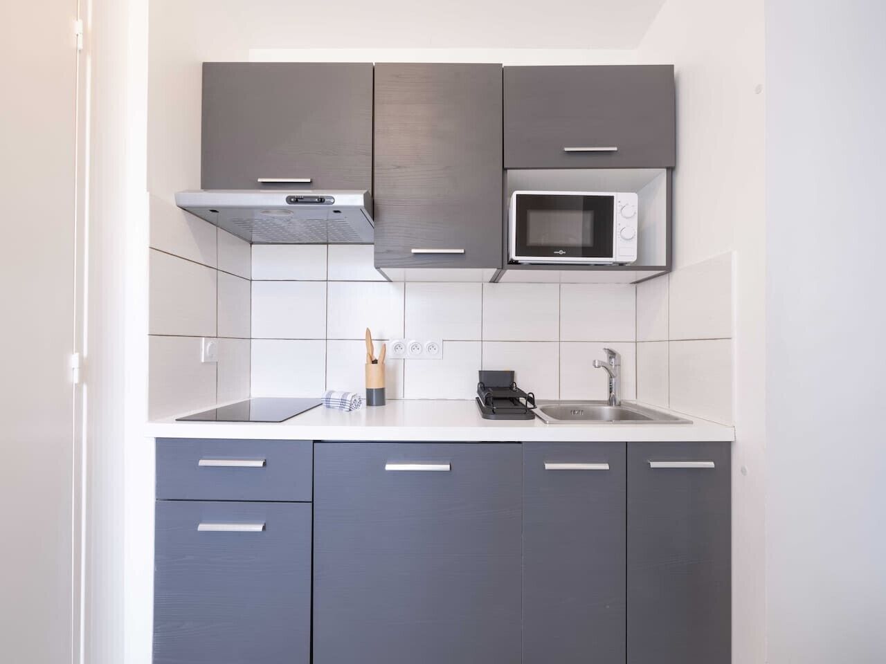 A compact kitchen with grey cabinets, a microwave, and a sink.