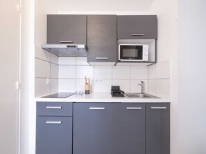 Una cocina compacta con gabinetes grises, un microondas y un lavamanos.