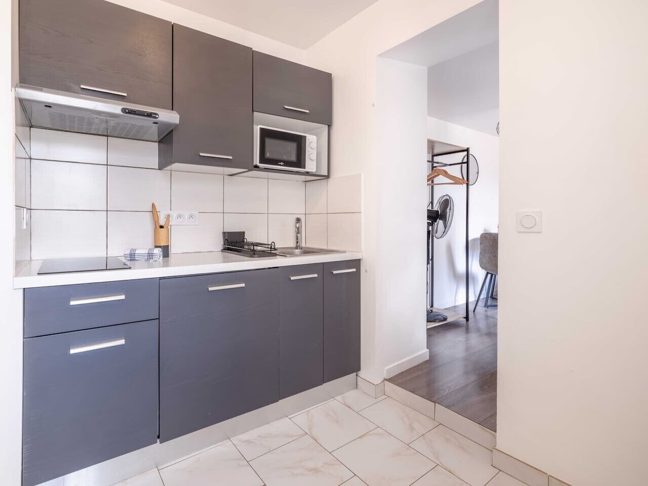 A modern kitchen with grey cabinets, a microwave, and a stainless steel range hood.