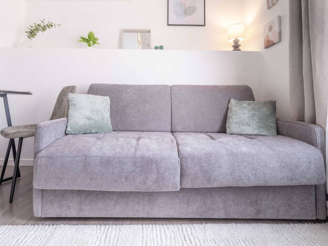 A grey sofa with two cushions, a small table with a chair, and a white rug.
