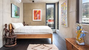 Quarto com cama, obras de arte, uma estátua e vista da cidade pela janela.