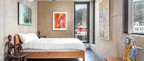 A bedroom with a bed, artwork, a statue, and a view of the city through a window.
