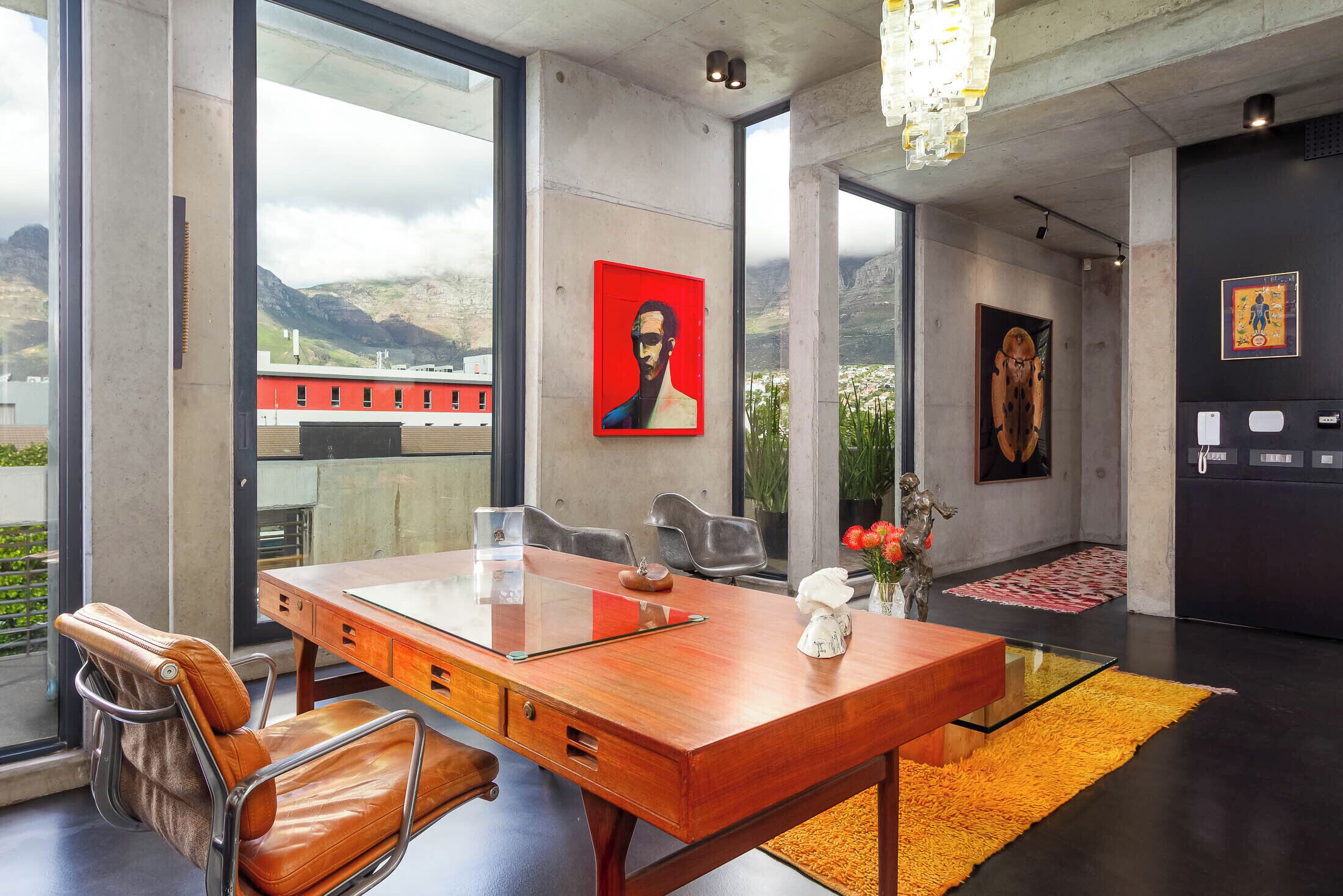A modern interior with a large wooden desk, leather chairs, a glass-top table, and artwork on the walls.