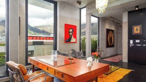 Um interior moderno com uma grande escrivaninha de madeira, poltronas de couro, uma mesa com tampo de vidro e obras de arte nas paredes.