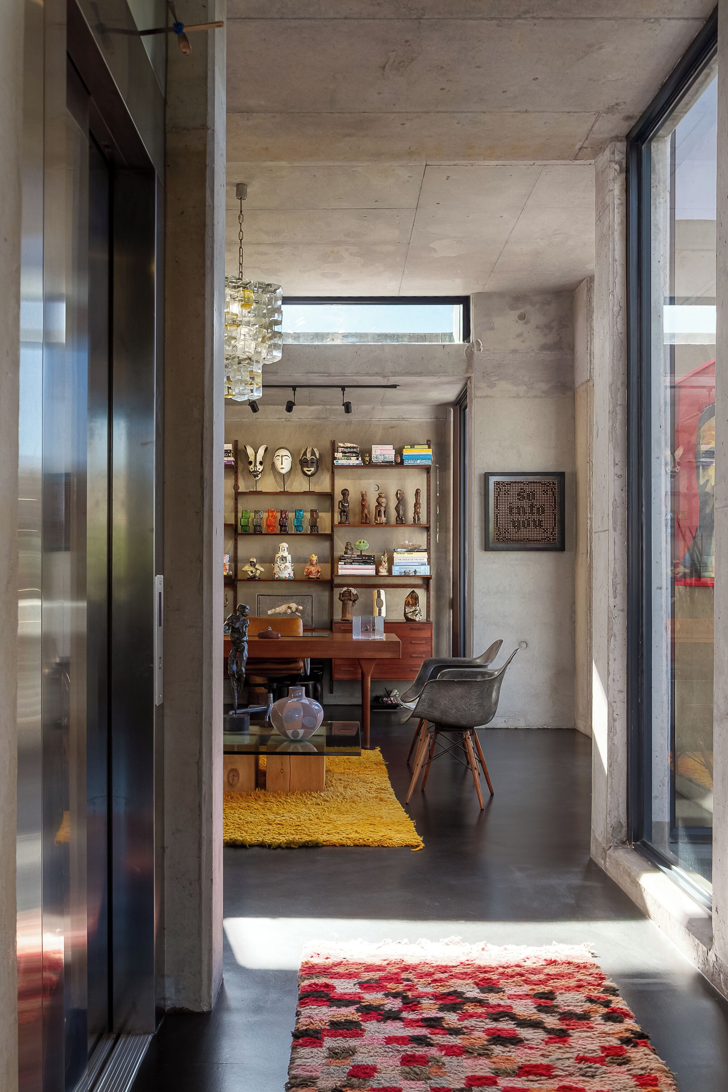 A modern interior with a concrete ceiling, a dining area with a wooden table and chairs, and a wall displaying various decorative items.