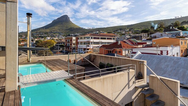 Piscina com deck de madeira e vista para uma cidade com edifícios e uma montanha ao fundo.