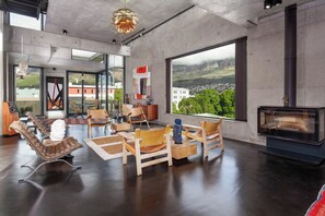 Uma sala de estar ampla com uma lareira grande, assentos confortáveis e vista para uma cidade por grandes janelas.