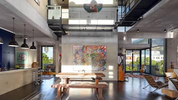 A spacious interior with a high ceiling, a large abstract painting, a wooden table, and a view of the outside through large windows.