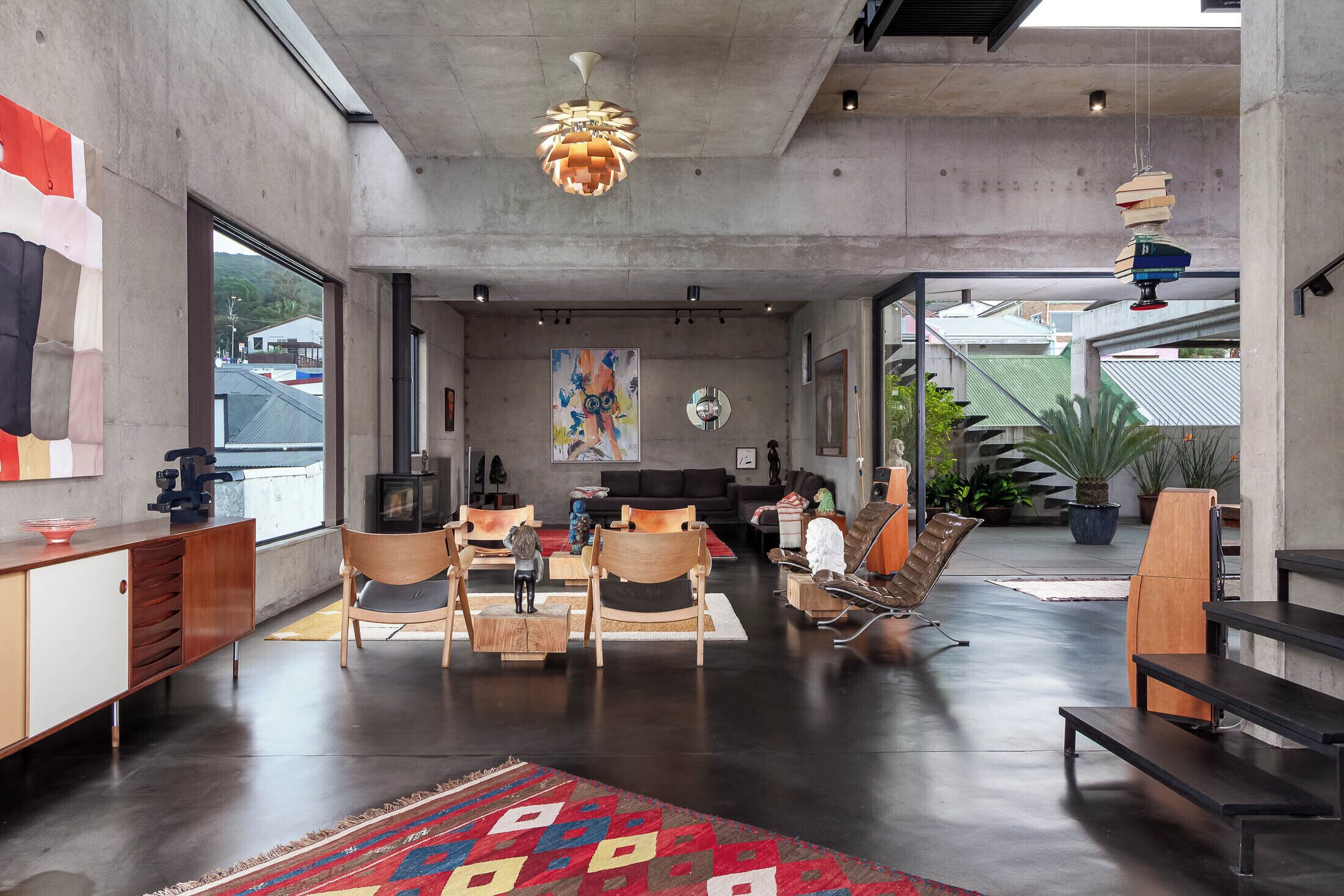 A modern interior with a sofa set, wooden chairs, a patterned rug, and a hanging light fixture.