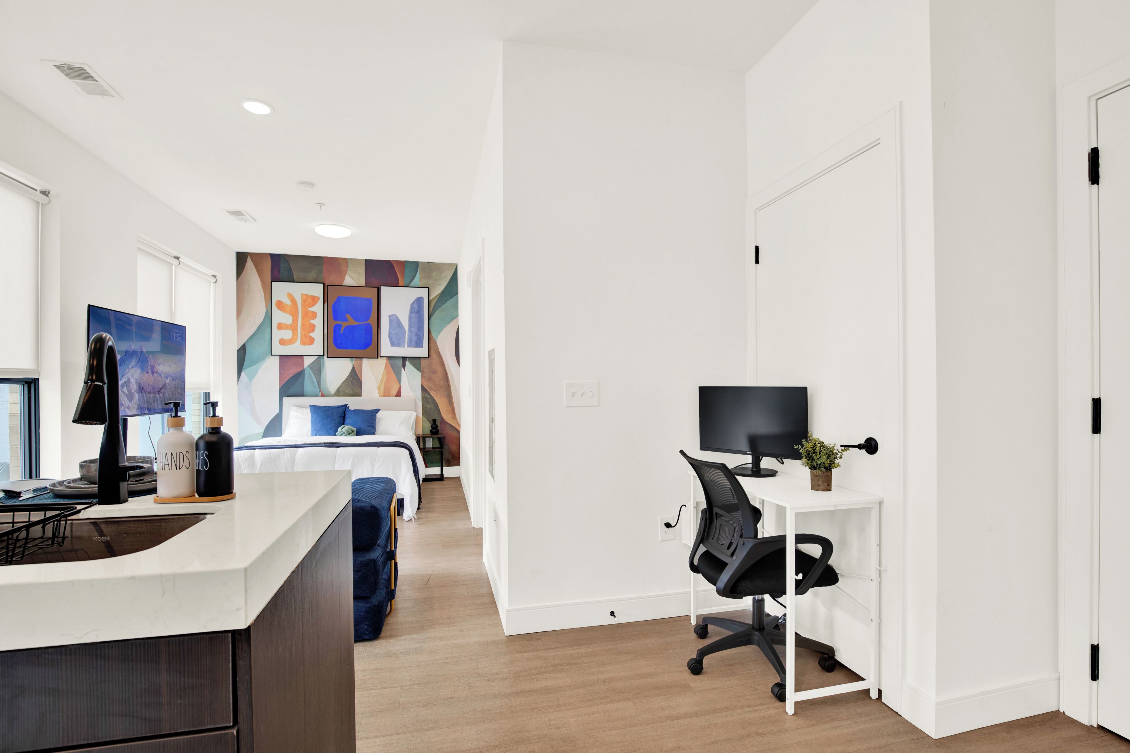 A modern hotel room with a large bed, a desk with a computer, a TV, and a bathroom with a shower and toilet.