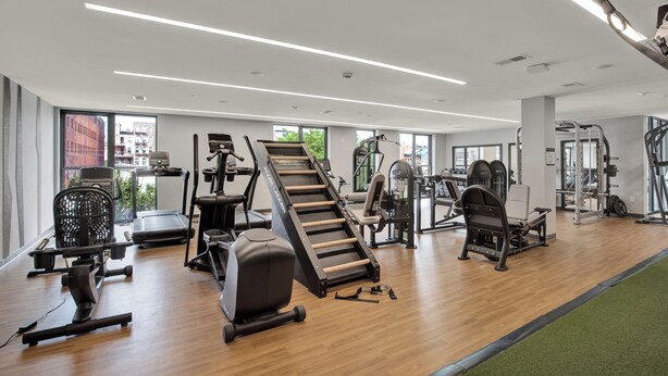 Une salle de sport moderne équipée de divers appareils d’exercice, dotée de grandes fenêtres et d’un plancher en bois.