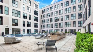 Un espace piscine aménagé sur le toit, avec des chaises longues, un barbecue et une vue sur la façade de l’immeuble.